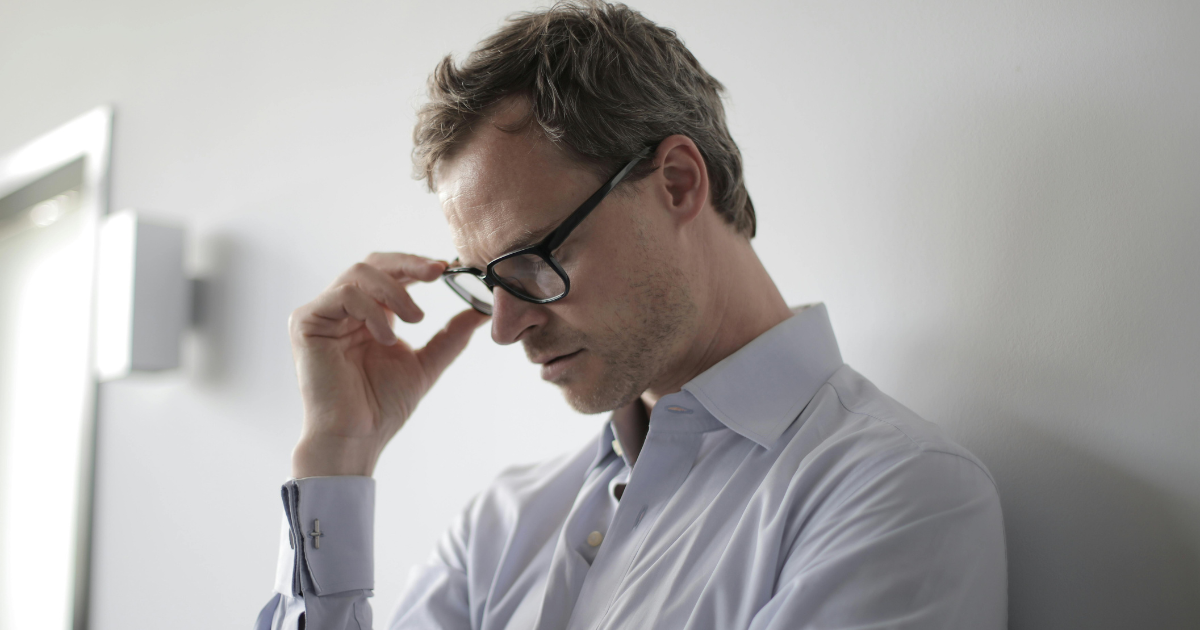 Anxious man in glasses, potential relief with Bupropion for anxiety symptoms. Light blue shirt, contemplative pose.