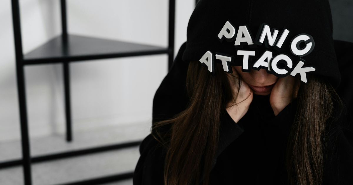 Woman experiencing panic attack symptoms. Black hoodie with "PANIC ATTACK" letters. Mental health and anxiety management.