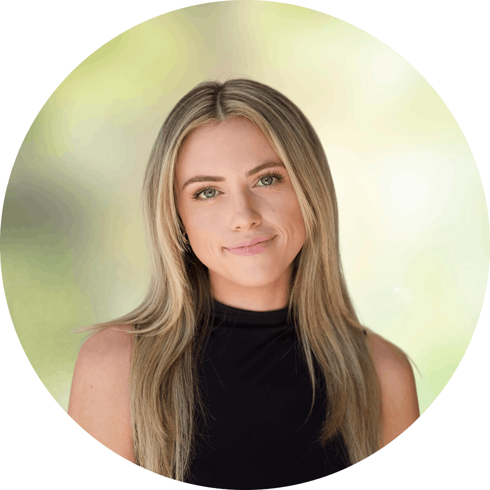 Portrait of a smiling woman with long blonde hair wearing a black sleeveless top, outdoors, blurred greenery.